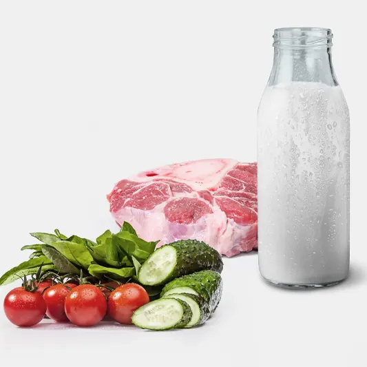 Fresh vegetables, a raw cut of meat, and a bottle of milk arranged on a light background.