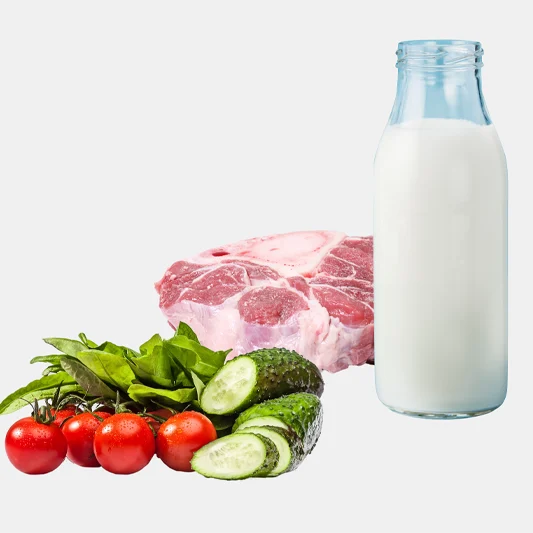 Bottle of milk next to raw meat, cherry tomatoes, leafy greens, and sliced cucumber on a light background.