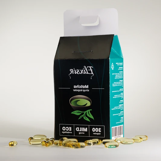 Mirrored image of Elixsir Matcha syrup capsules box with green side panel and golden capsules scattered around on a light surface.