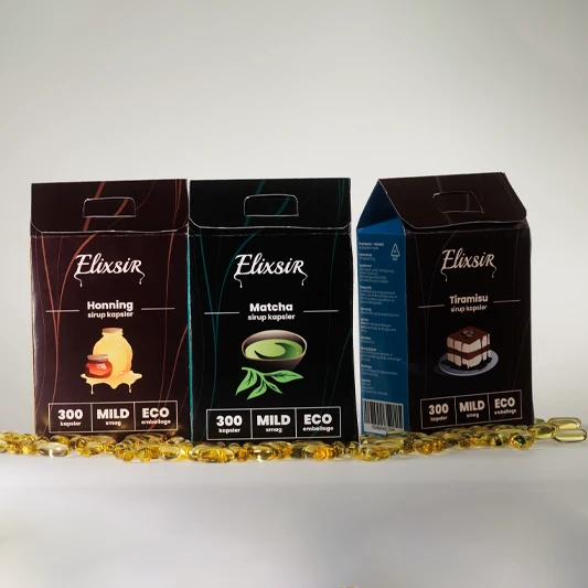 Three Elixsir syrup capsule boxes—Honey, Matcha, and Tiramisu—standing in a row with golden capsules scattered in front on a neutral background.