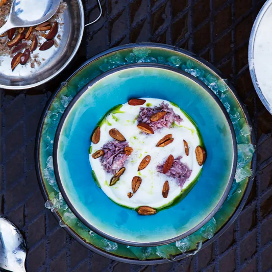 Artistic plated dish in a blue bowl on crushed ice, topped with seeds, herbs, and a creamy white base.