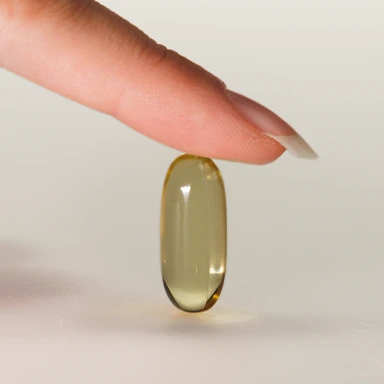 Close-up of a hand with manicured nails gently holding a translucent syrup capsule upright on a light surface.