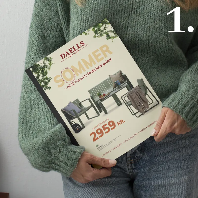 Person holding the Daells Bolighus summer catalogue featuring garden furniture and the headline “SOMMER – alt til haven til faste lave priser”.