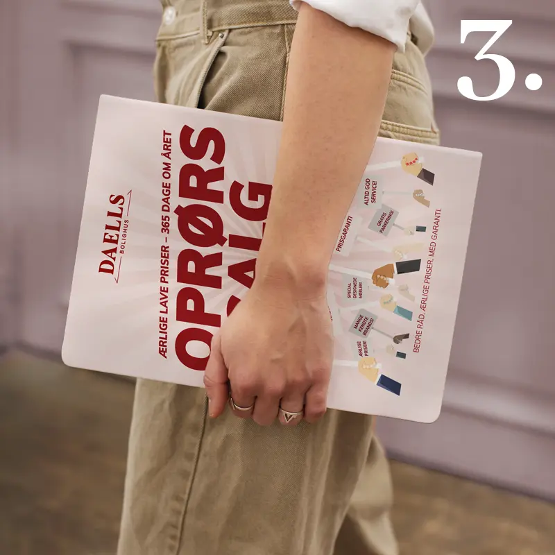Person holding a Daells Bolighus “Oprørssalg” catalogue with bold red typography promoting year-round low prices.