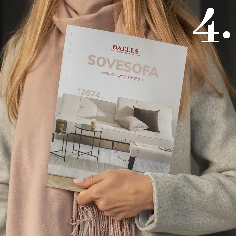 Person holding a Daells Bolighus sofa catalogue with the title “SOVESOFA – Find den perfekte til dig” and a beige sofa on the cover.