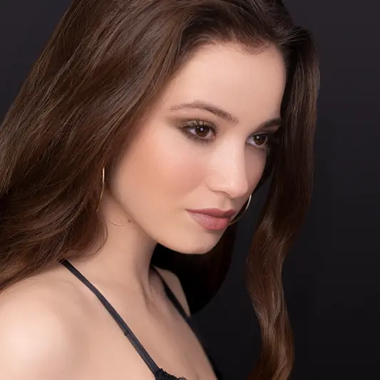 Retouched portrait of a brunette woman, nearly identical pose as before, but with enhanced makeup, smoother skin, and subtle color grading.