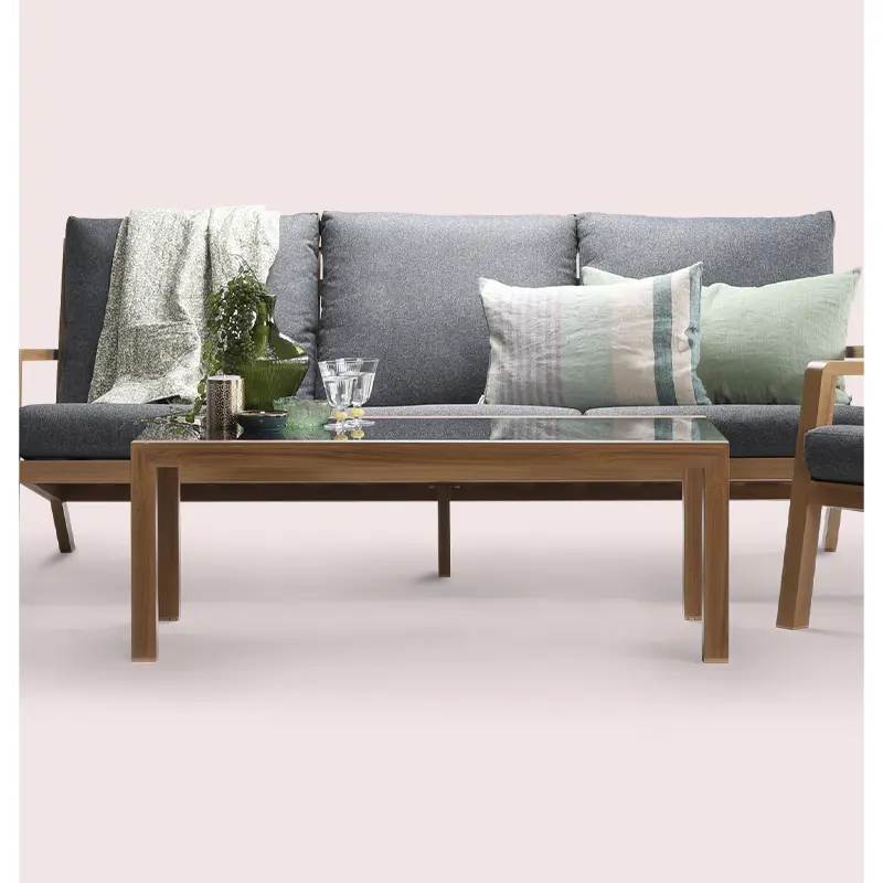 Styled shot of a grey outdoor sofa set with green accents and decorative props, placed against a soft pink background.