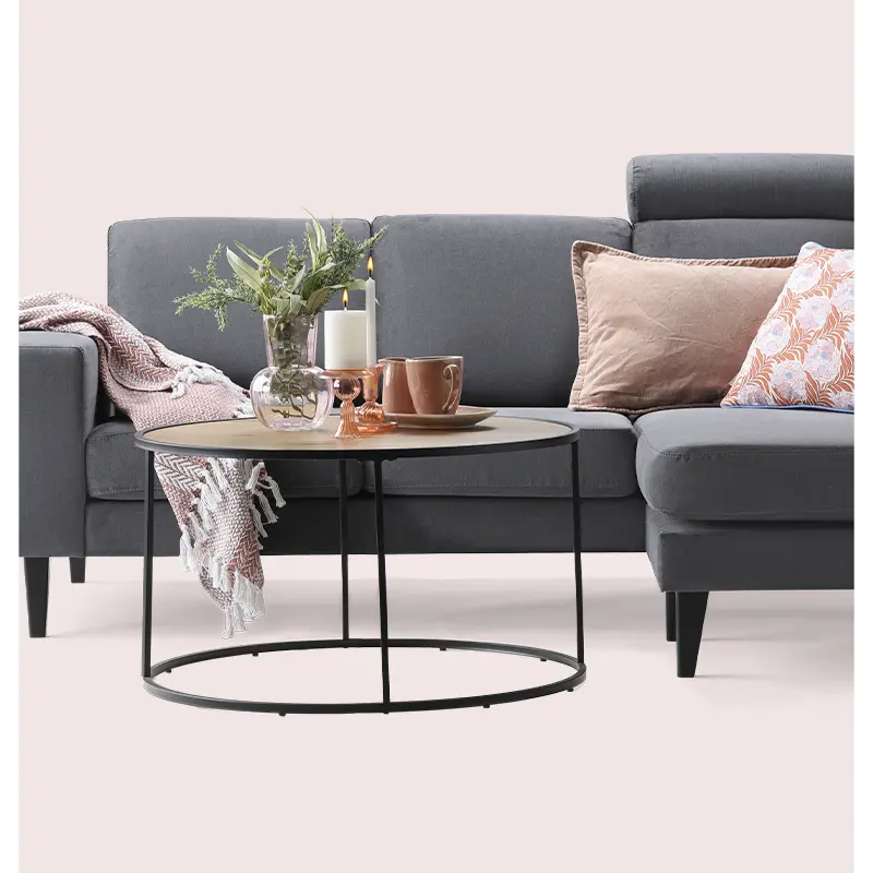 Dark grey sofa styled with warm pink cushions and copper accents, paired with a round coffee table on a pale pink background.